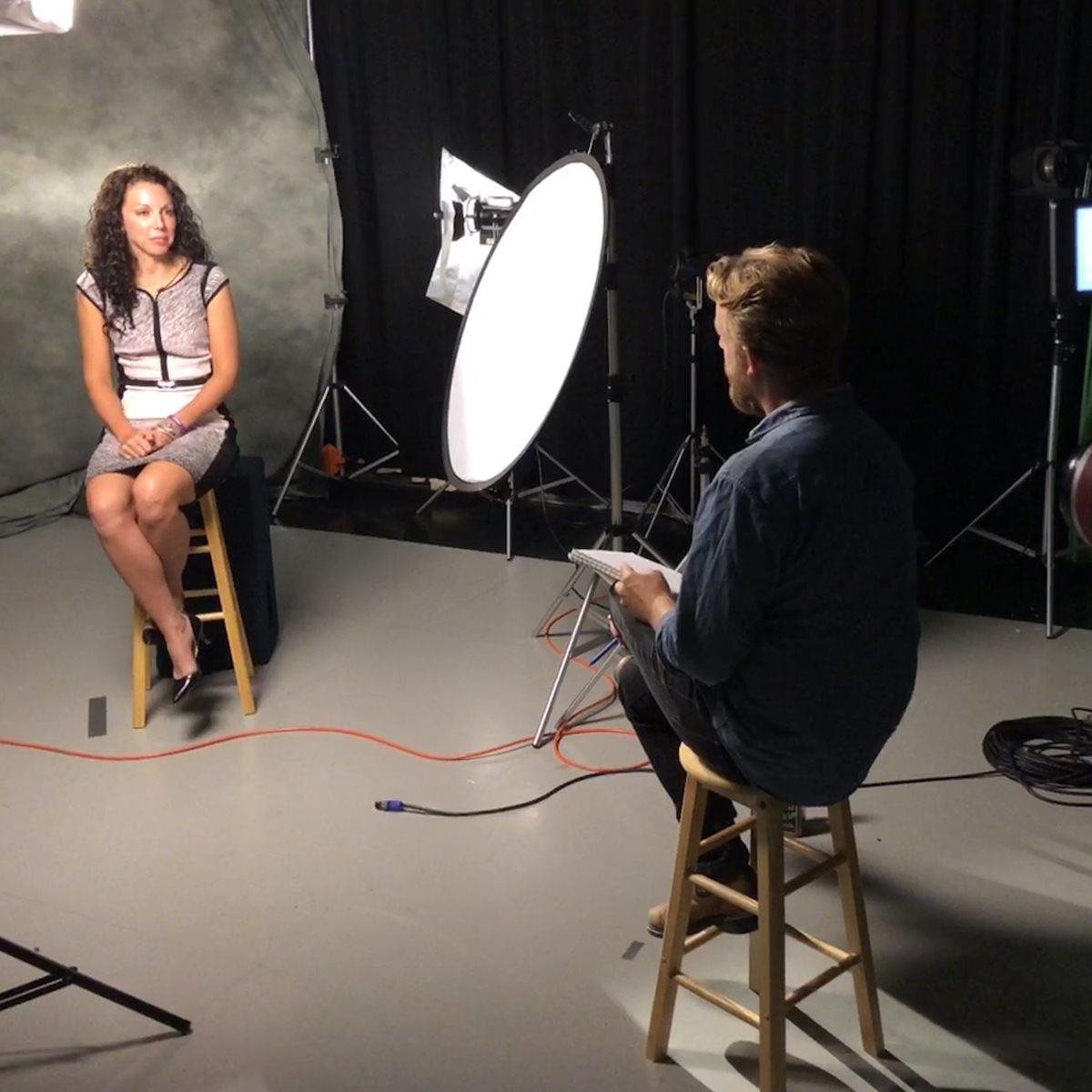 A woman sits in a photo studio, with an interviewer sitting off camera